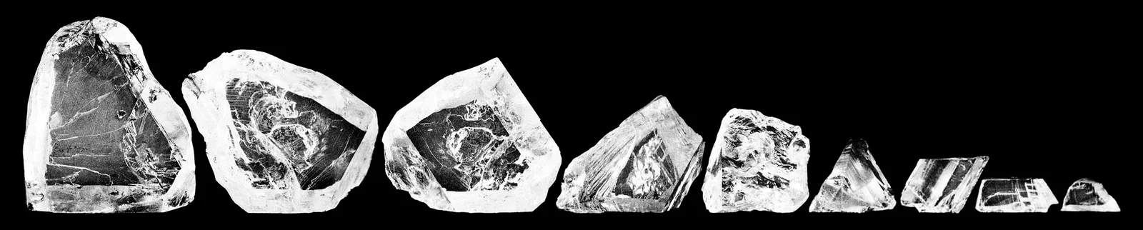 Nine rough diamond pieces of decreasing size photographed in a row against a black background, the largest at left, all cleaved from the Cullinan rough diamond