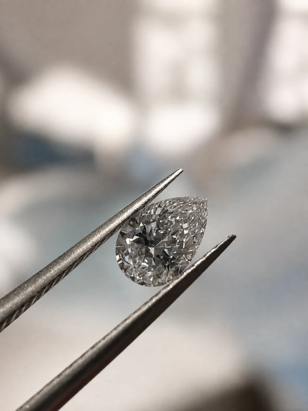 A 0.23 carat pear shaped diamond held in tweezers