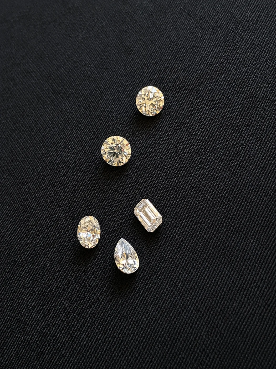 Five natural diamonds — two rounds, an oval, a pear and an emerald cut — laid out together on black fabric