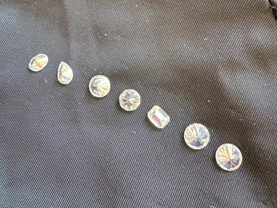 The same seven stones in the same order in ordinary light: seven colourless diamonds, with nothing to tell them apart.